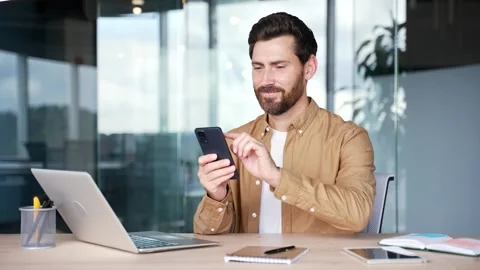 Businessman is using browsing mobile phone while sitting at desk at workplace  Stock Footage 325513439
