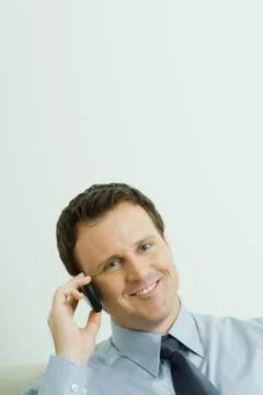 Businessman using cell phone, head tilted, smiling at camera Stock Photos