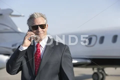 Businessman Using Cell Phone With Private Jet In Background Stock Photos