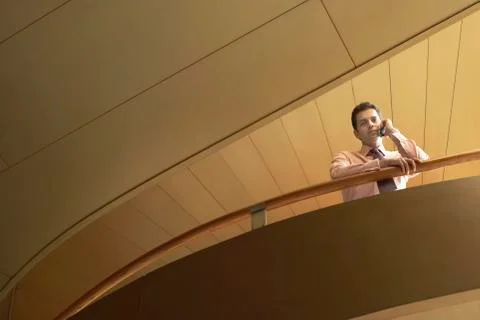 Businessman Using Cellphone While Leaning On Railing In Office Stock Photos