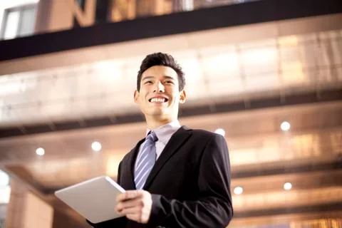 A businessman using a digital tablet outside an office building at night Fotos de archivo