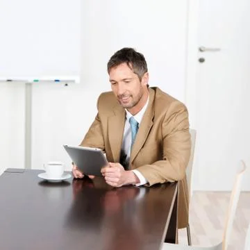 Businessman using digital tablet while sitting on desk Stock Photos
