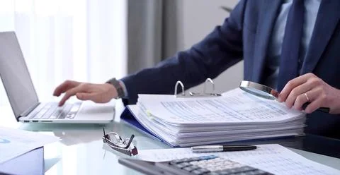 Businessman using a laptop computer and magnifying glass while analyzing Stock Photos