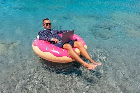 Businessman using laptop computer on an inflatable donut in the sea. Foto stock