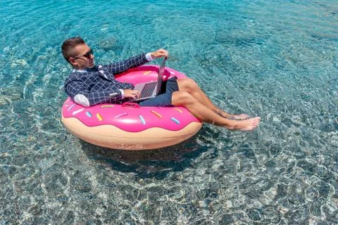 Businessman using laptop computer on an inflatable donut in the sea. Stock Photos