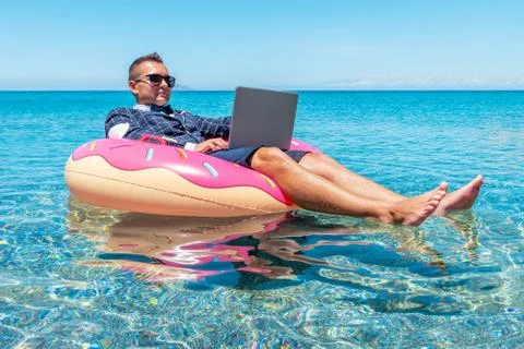 Businessman using laptop computer on an inflatable donut in the sea. Foto stock
