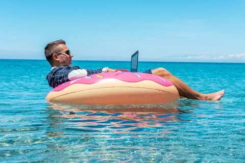 Businessman using laptop computer on an inflatable donut in the sea. Stock Photos