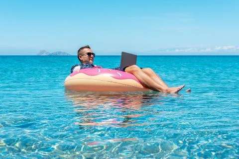 Businessman using laptop computer on an inflatable donut in the sea. Stock Photos