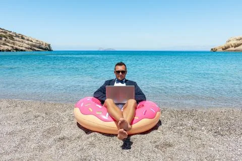 Businessman using laptop computer on inflatable donut on tropical beach. Stock Photos