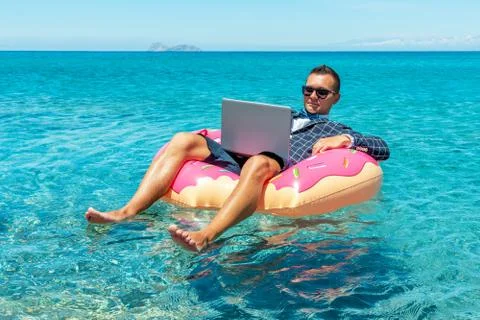 Businessman using laptop computer on an inflatable donut in the sea. Stock Photos