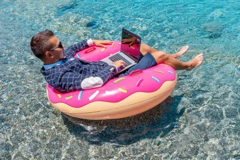 Businessman using laptop computer on an inflatable donut in the sea. Foto stock