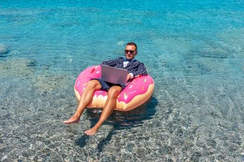 Businessman using laptop computer on an inflatable donut in the sea. Stock Photos