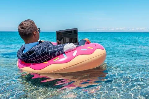 Businessman using laptop computer on an inflatable donut in the sea. Stock Photos