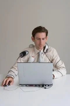 Businessman using laptop covered in computer equipment Stock Photos