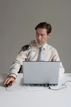 Businessman using laptop covered in computer equipment Stock Photos