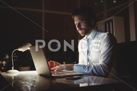 Businessman Using Laptop At Night In The Office