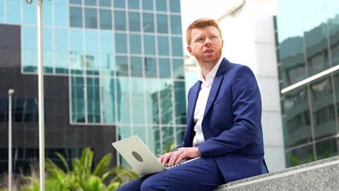 Businessman using laptop sitting outside an office block Stock Footage 274430782