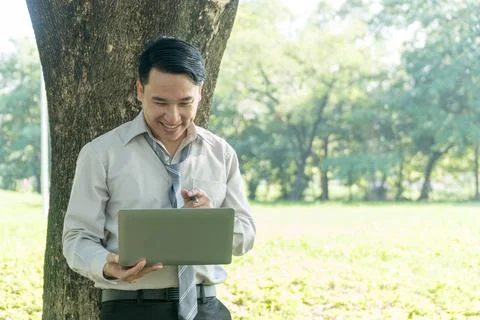 Businessman using laptop under the tree in the park. Smile happily of middle- Stock Photos