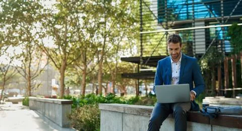 Businessman using a laptop while sitting outside his office building Stock Photos