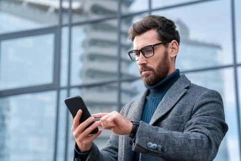 Businessman using mobile app standing outside office in urban city street Stock Photos