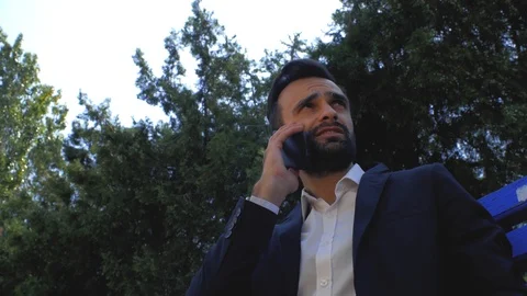 Businessman using a mobile phone in a park on a bench. man talking on a cell Stock Footage 113898602