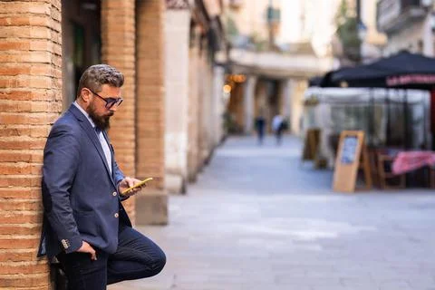 Businessman using a mobile phone while leaning on a column outdoors in the Stock Photos