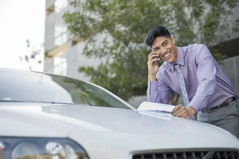 Businessman using mobile phone while leaning on car Stock Photos