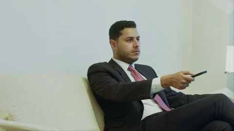 Businessman using remote control while watching TV at his hotel room Stock Footage 80360709