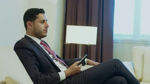 Businessman using remote control while watching TV at his hotel room Stock-Footage 80360801