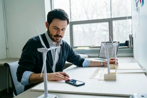 Businessman using smart phone while arranging wind turbine models on desk Stock Photos