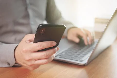 Businessman using smartphone and computer laptop while working from home to c Stock Photos