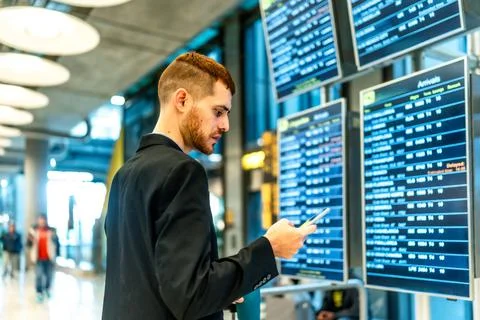 Businessman using smartphone checking flight information on airport display 写真素材