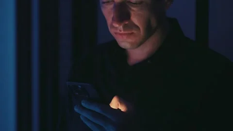 Businessman using smartphone in a dimly lit room at night, screen light casting Stock Footage 312748918