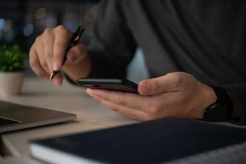 Businessman using a smartphone while holding a pen, multitasking between mo.. Stock Photos