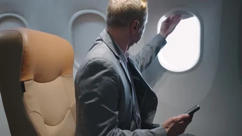 Businessman using smartphone while travels on airplane open window looking view Stock Footage 240813632
