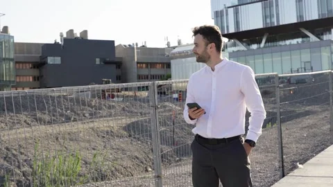 Businessman using smartphone while walking near construction area. Stock Footage 244246259