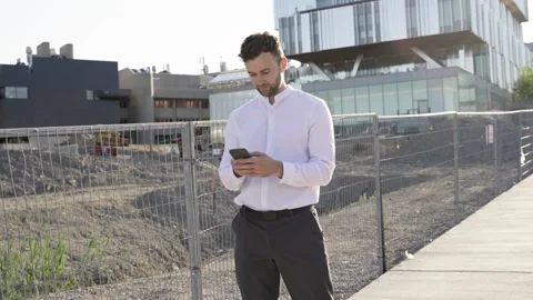 Businessman using smartphone while walking near construction area. Stock Footage 244246337