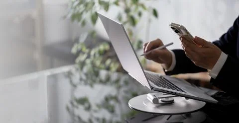 Businessman using smartphone while working on laptop computer on office table 写真素材