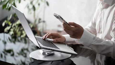 Businessman using smartphone while working on laptop computer on office table 写真素材