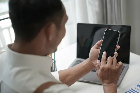 Businessman using smartphone while working on laptop at home office, concep.. Fotos Stock