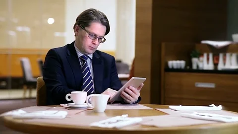 A businessman using a tablet and drinking a coffee in a hotel cafe. Slow motion. Stock Footage 70625407