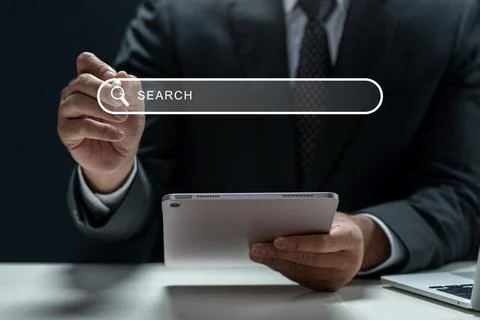 Businessman using a tablet and touching a search engine bar icon. Laptop on.. Stock Photos