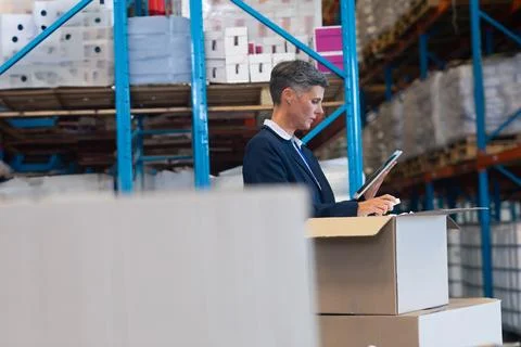 Businessman using tablet checking inventory in large warehouse with shelves, Fotos de archivo