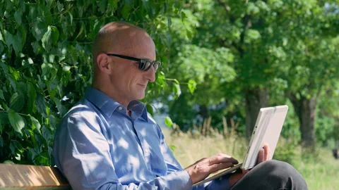 Businessman using tablet on park bench outdoors Stock Footage 339033454