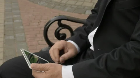 Businessman using tablet PC and sitting on a bench in the street close up Stock Footage 63564785