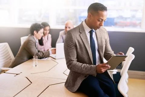 Businessman using a tablet with three colleagues seated behind him Stock Photos