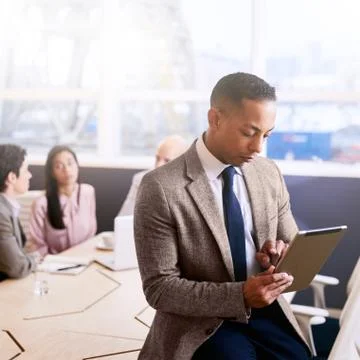 Businessman using a tablet with three colleagues seated behind him Stock Photos