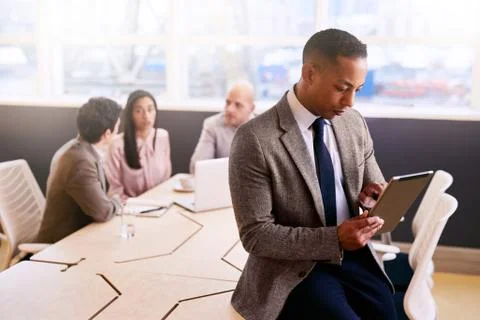 Businessman using a tablet with three colleagues seated behind him Fotos Stock
