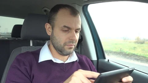 Businessman using a tablet while sitting inside car. Man with a tablet-pc in Stock Footage 83023811