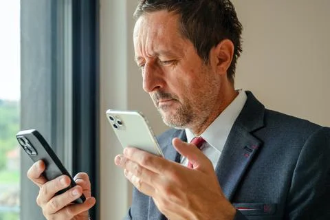 Businessman using two smartphones simultaneously, trying to synchronize dat.. Stock Photos